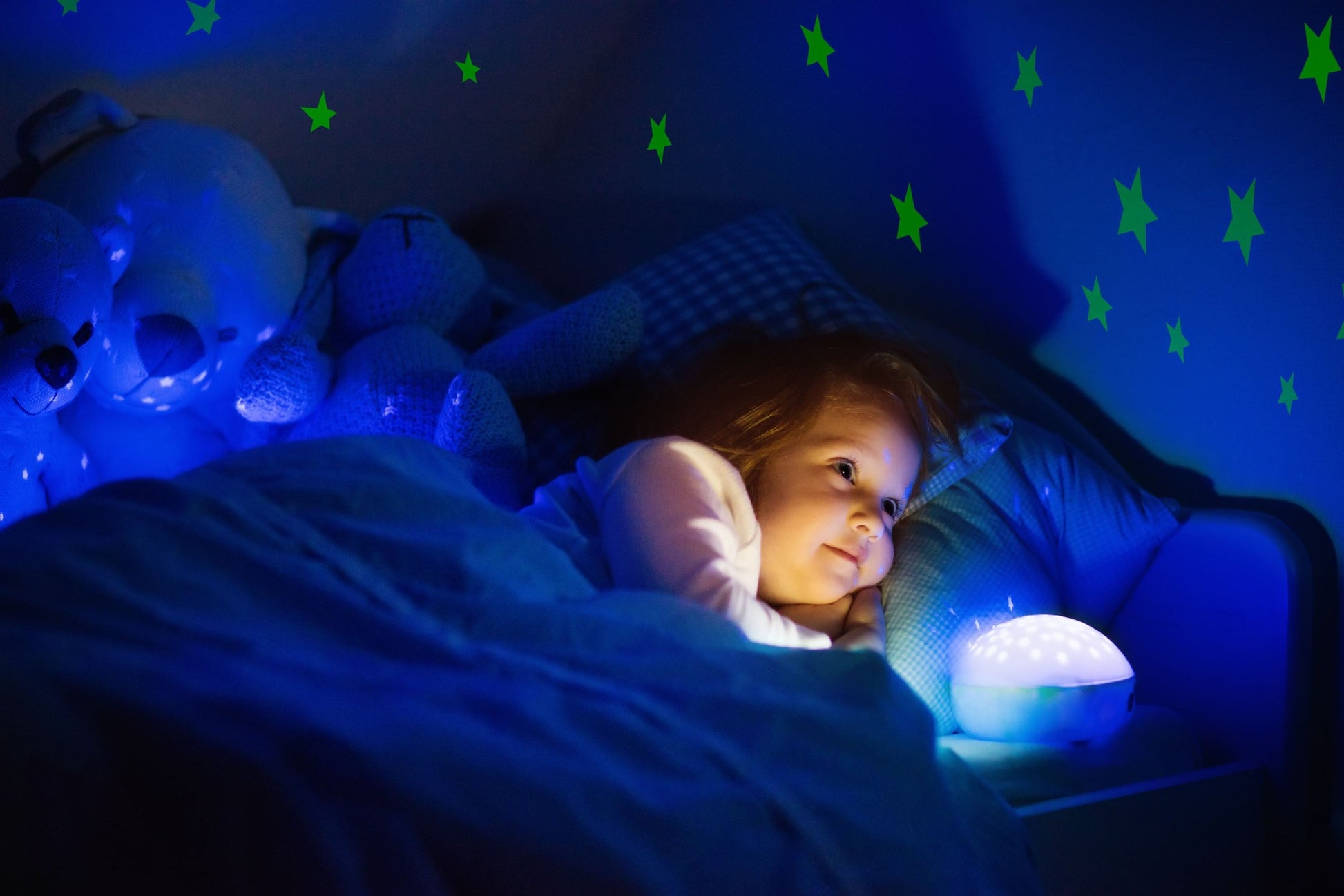 Girl with a bedtime light and stars on the wall glowing behind her